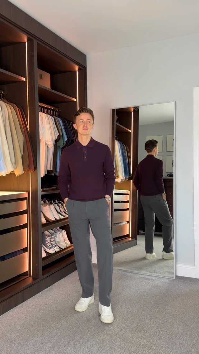 Man wearing a purple polo shirt, grey trousers, and white sneakers standing in a bedroom.