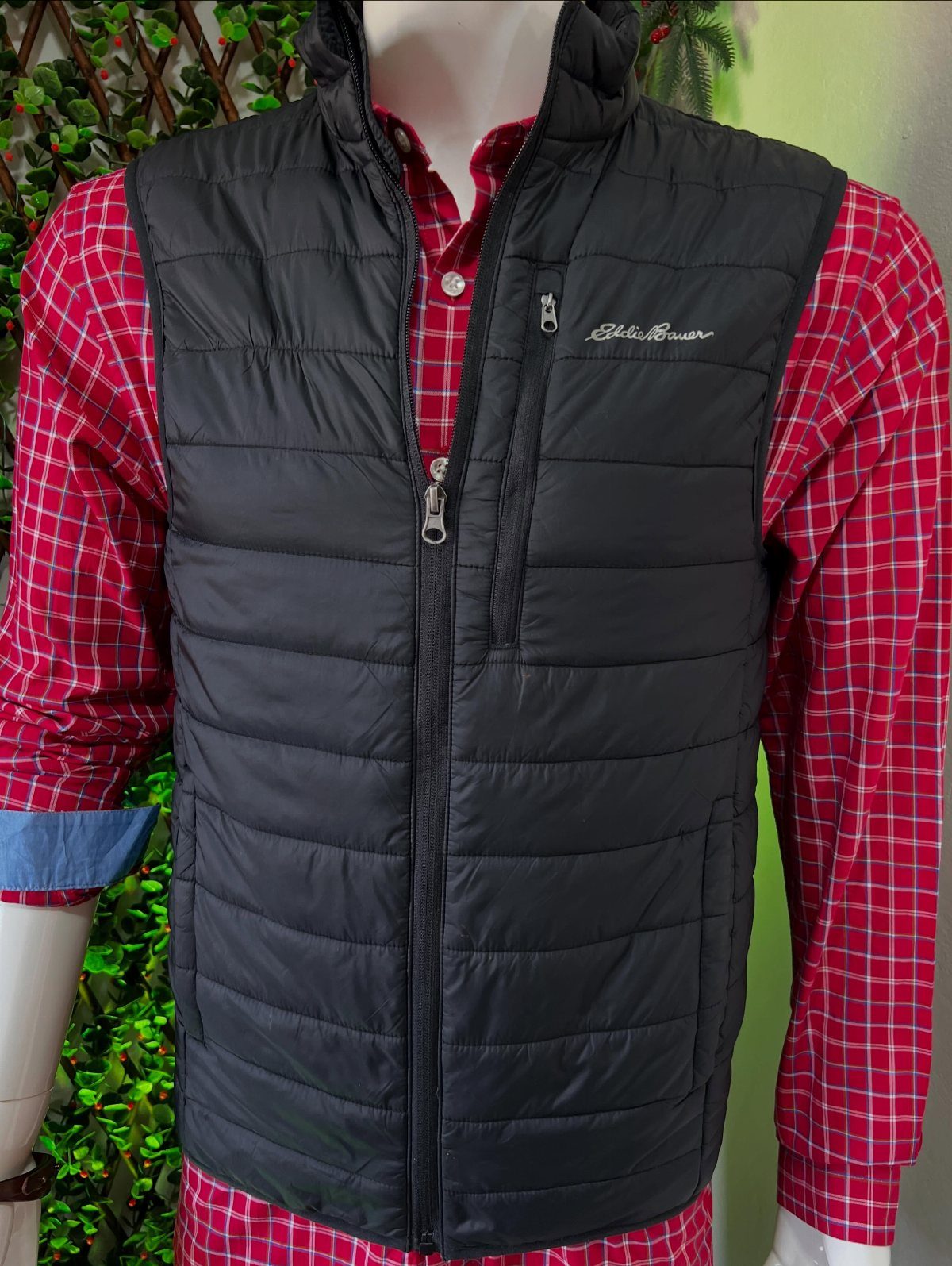 A black quilted puffer vest worn over a red checkered shirt on a mannequin.