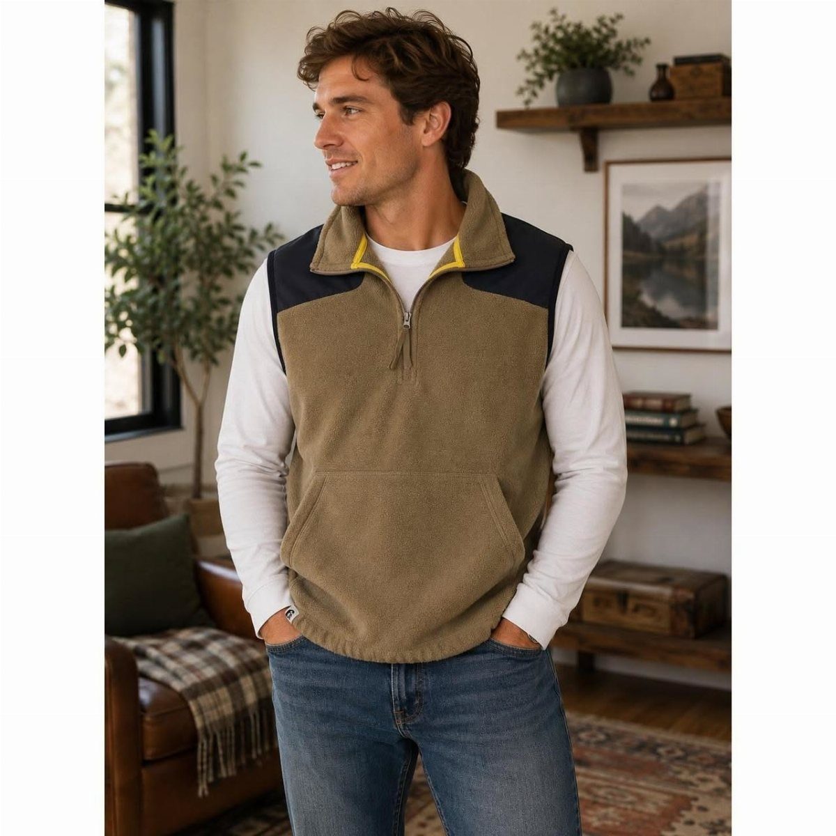 A man smiling while wearing a tan and navy blue fleece vest and blue jeans.