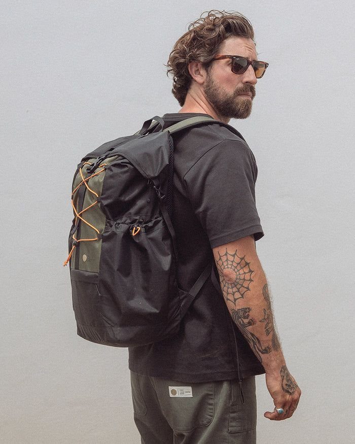 A man with tattoos and sunglasses wearing a black t-shirt and a black ripstop backpack.