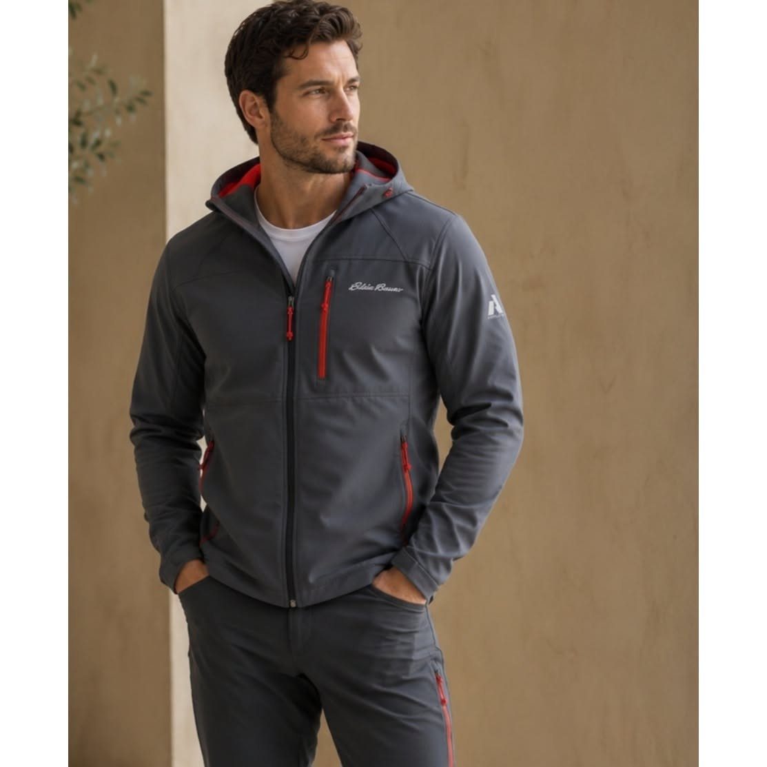 Man wearing a grey Eddie Bauer hooded soft shell jacket with red zipper details.