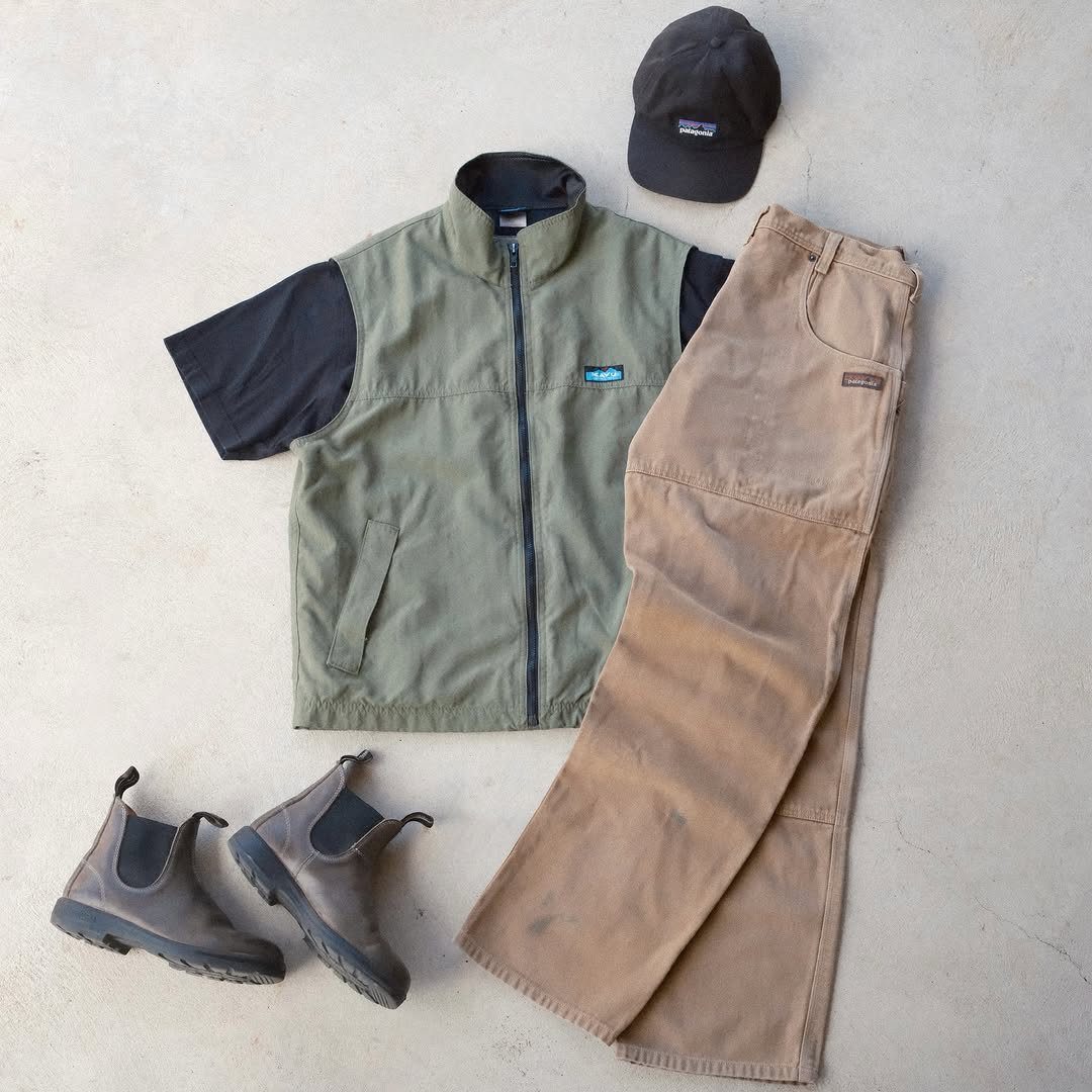 An outdoor clothing ensemble featuring a green vest, tan pants, grey boots, and a black cap.
