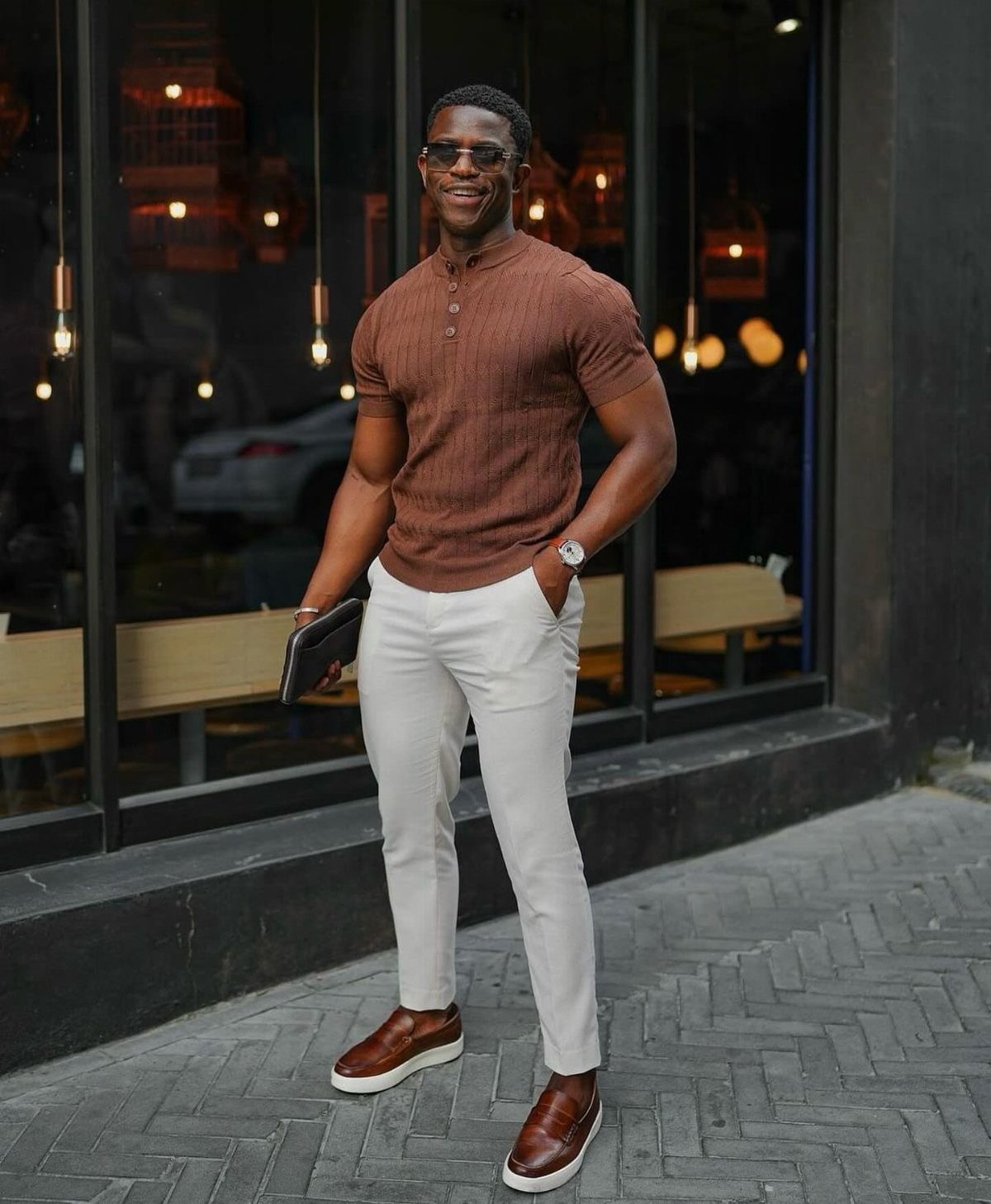 A man in a brown henley shirt and white trousers standing on a city sidewalk.
