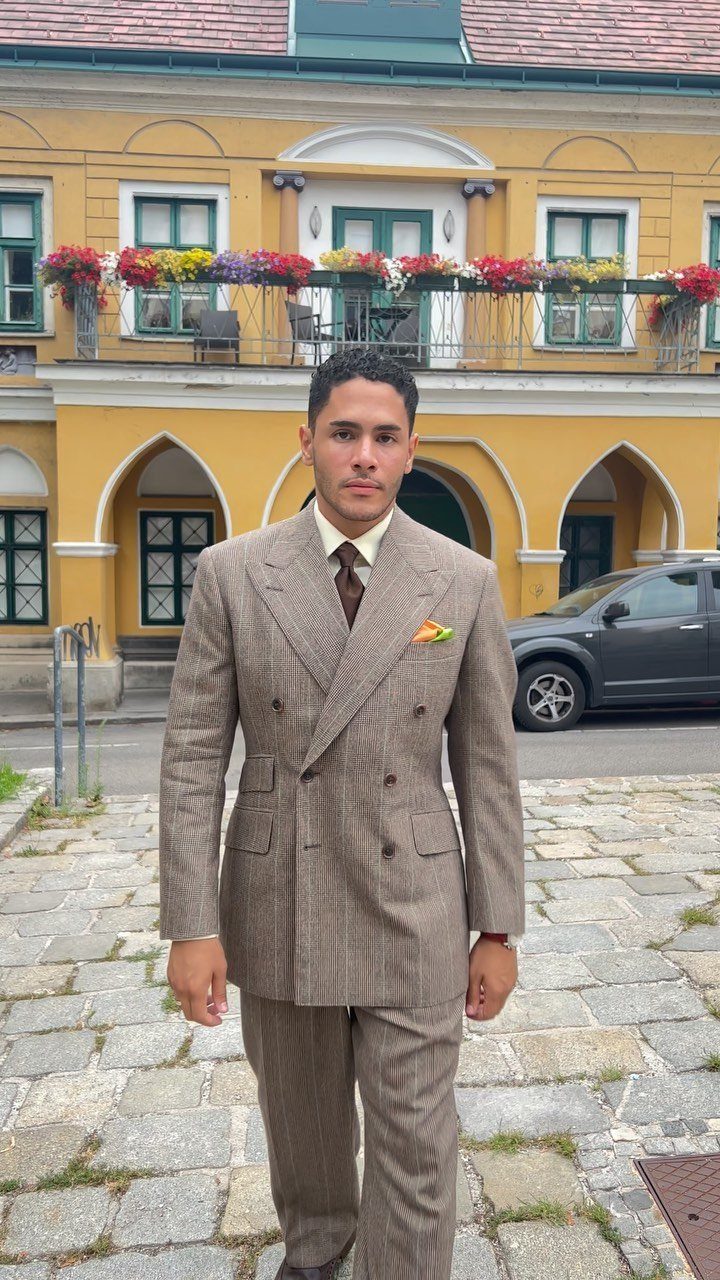 Man wearing a tan double-breasted suit with a subtle checked pattern standing outdoors.