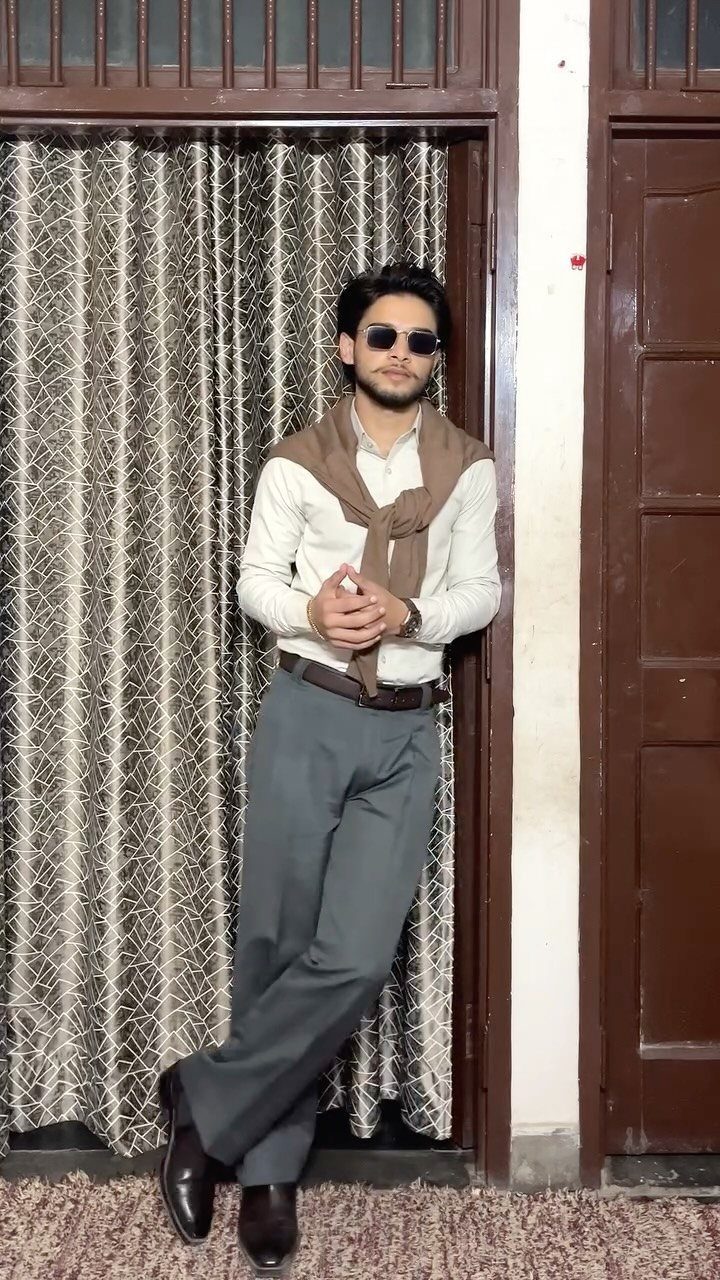 A man in a white shirt and grey trousers posing against a doorway.