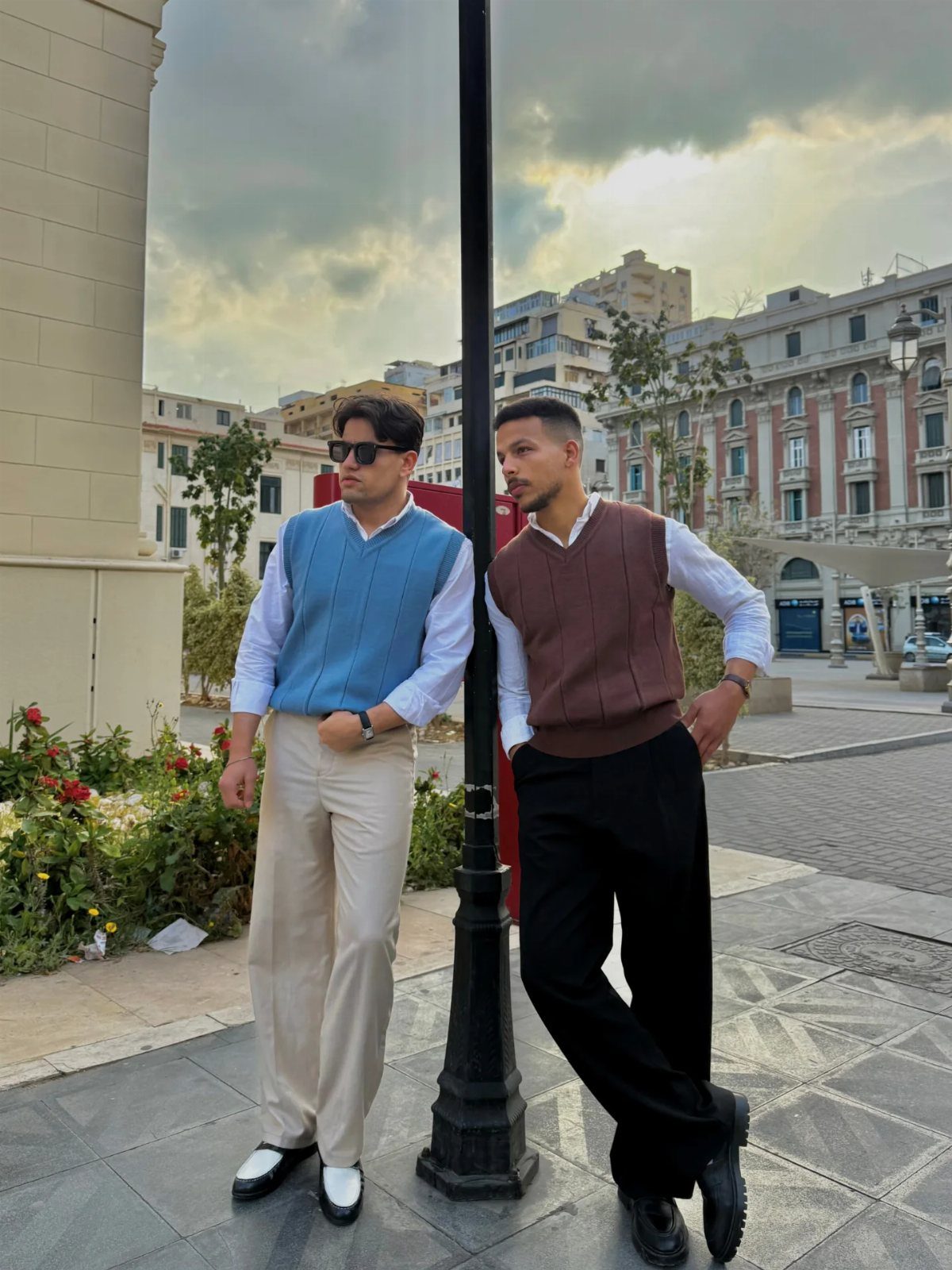 Two men posing in stylish sweater vests layered over white dress shirts and trousers.