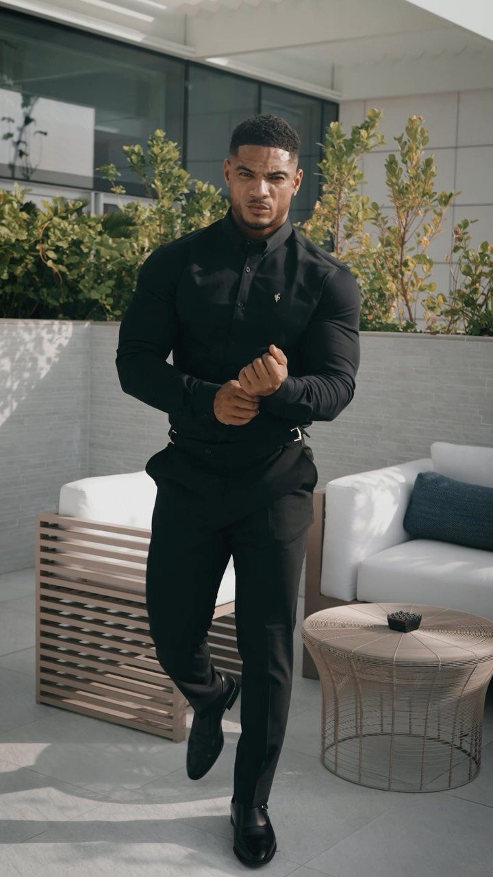 Man in a black long-sleeved button-down shirt and black trousers standing on a patio.