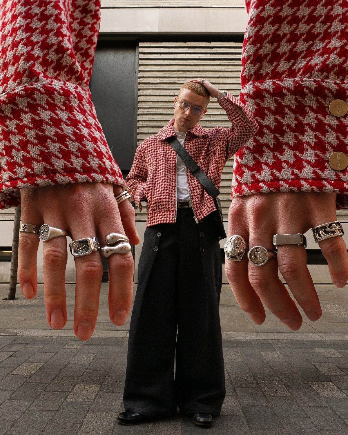 Man in checkered shirt standing between two giant hands adorned with large silver rings.