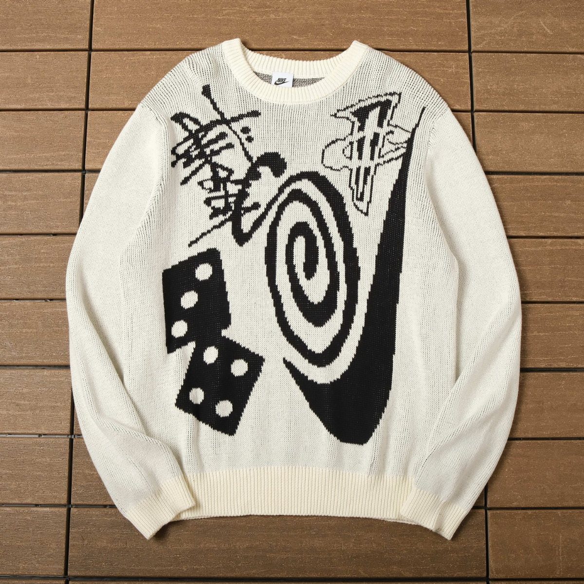 White knit sweater featuring large black graphic patterns laid on a wooden surface.