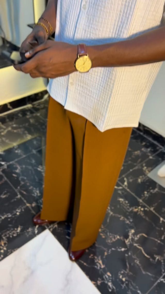A person wearing a white textured shirt and brown wide-leg trousers with a gold watch.