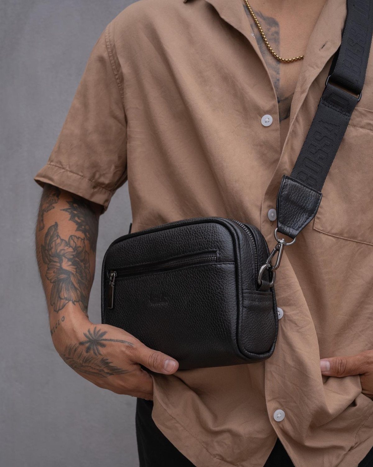 A person wearing a tan shirt with a black leather crossbody bag worn over the shoulder.