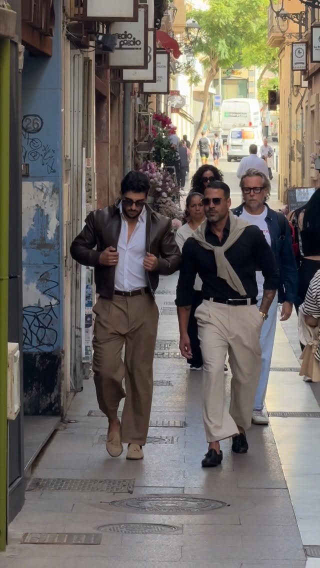 Two men walking down a narrow street wearing stylish European casual outfits.