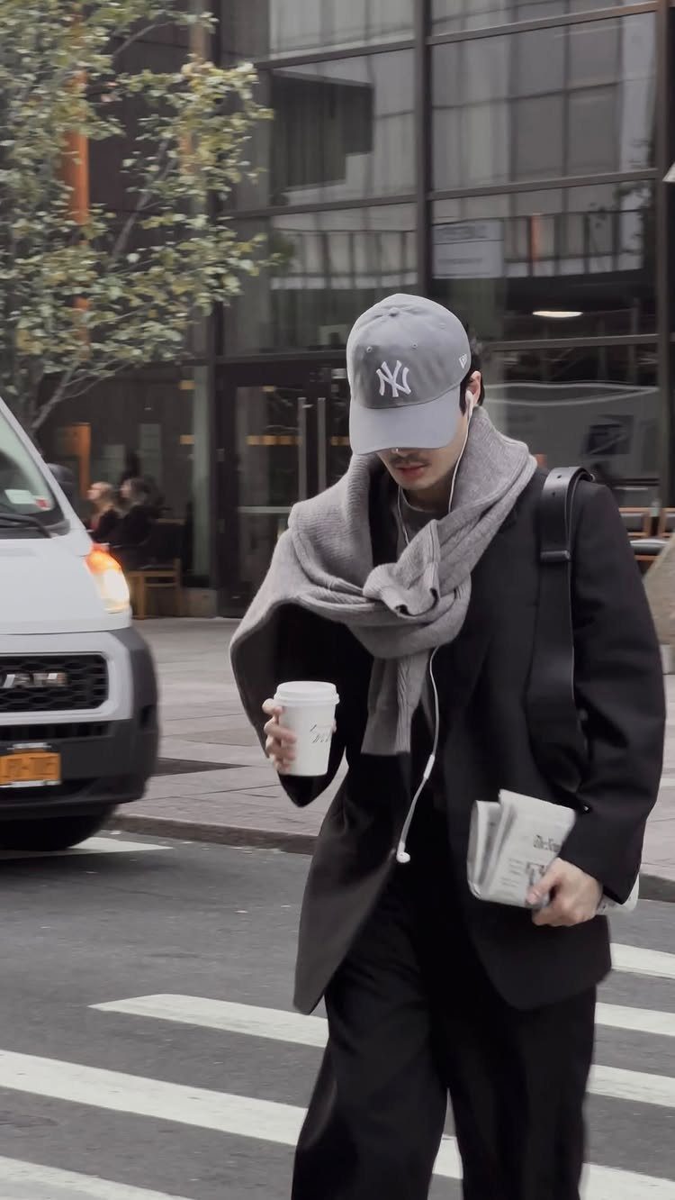 A person in a black blazer and grey baseball cap walking through a city street.