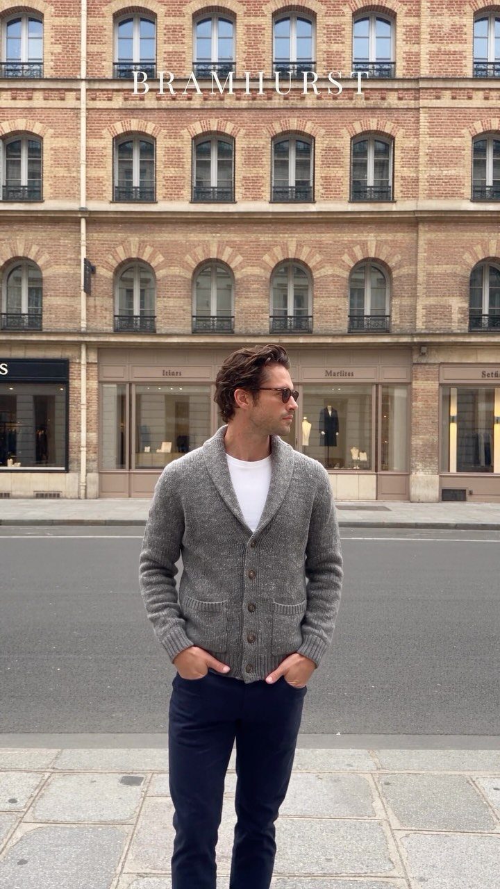A man in a grey cardigan and dark trousers standing on a city street.