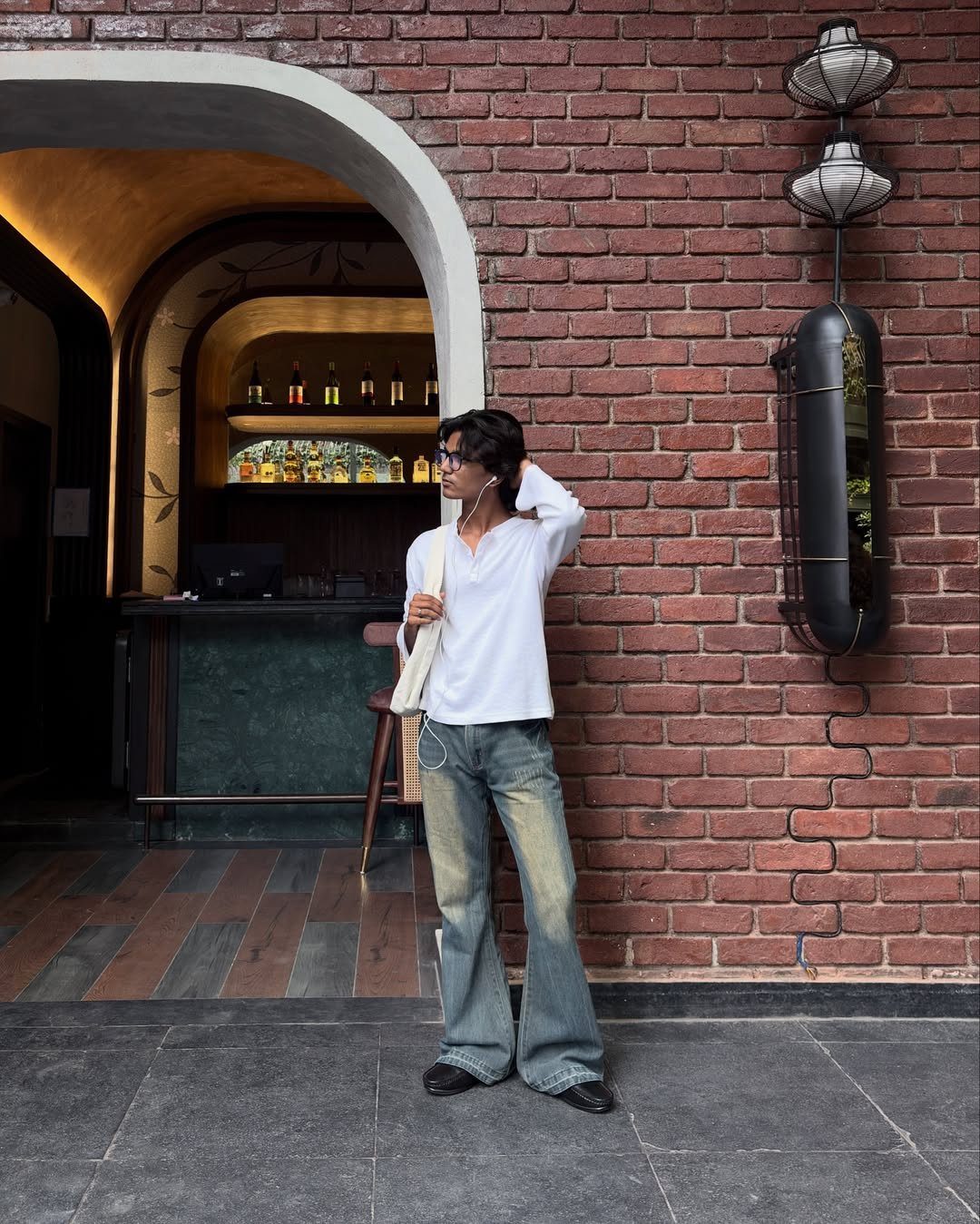 A person wearing a white shirt and flared denim jeans standing against a brick wall.