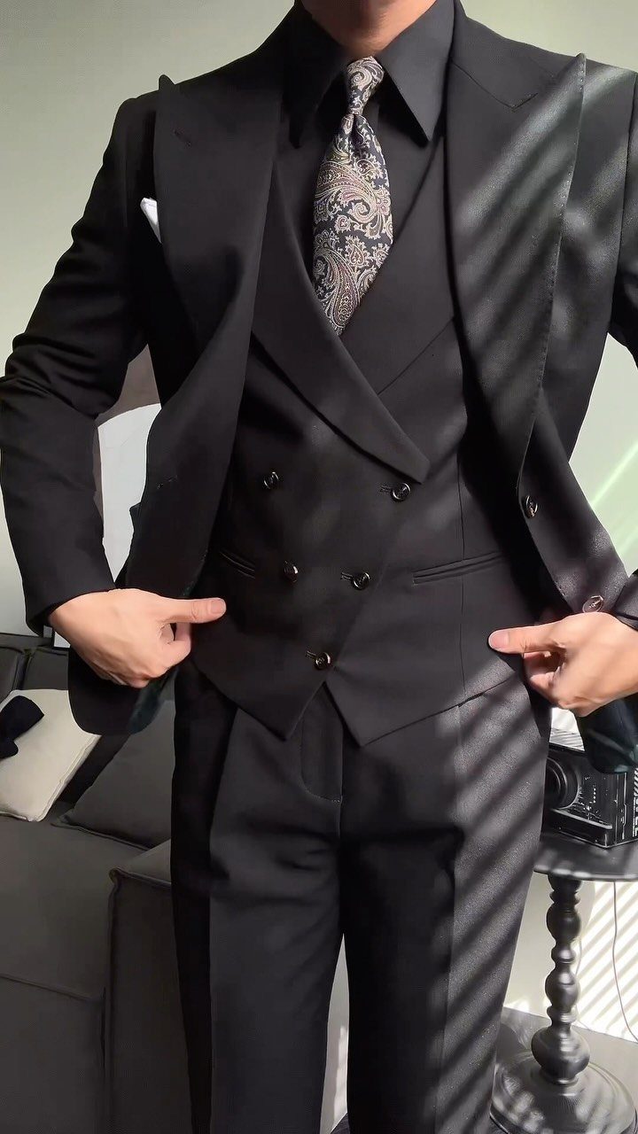 A man wearing a black three-piece suit with a patterned tie and black shirt.