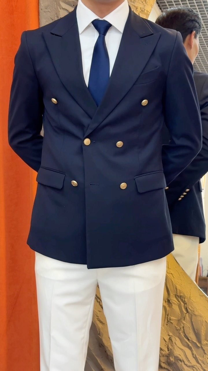 Man wearing a navy double-breasted blazer with gold buttons, white shirt, and white trousers.