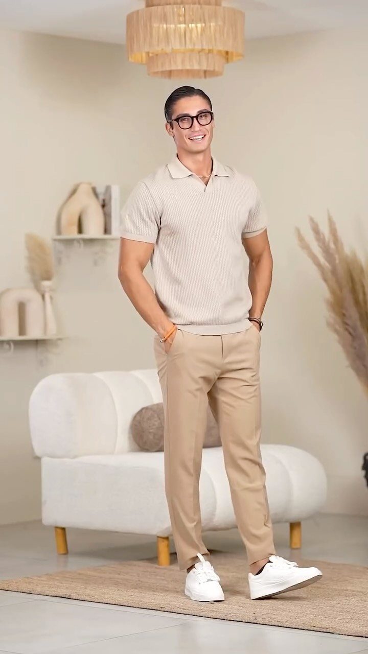 A smiling man in a beige polo shirt and tan trousers standing in a modern living room.