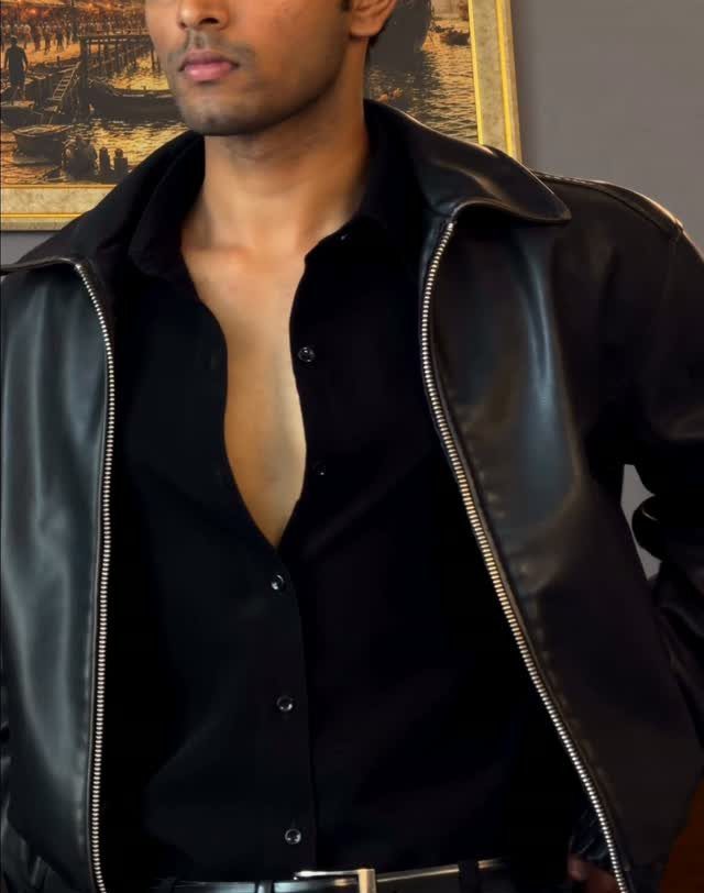 A man wearing a black leather jacket over an unbuttoned black shirt.