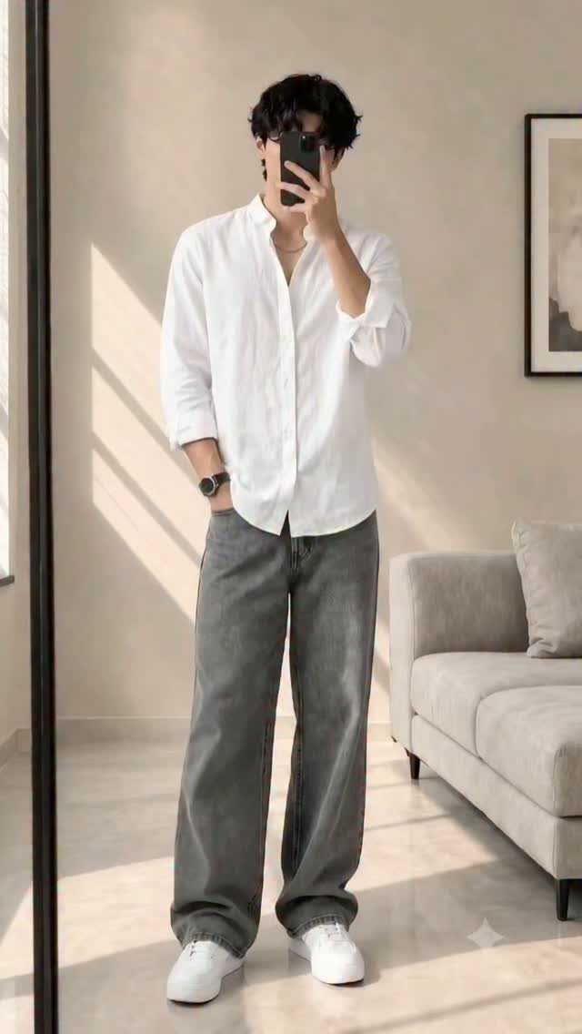 A man posing in a white button-down shirt and wide-leg grey trousers.