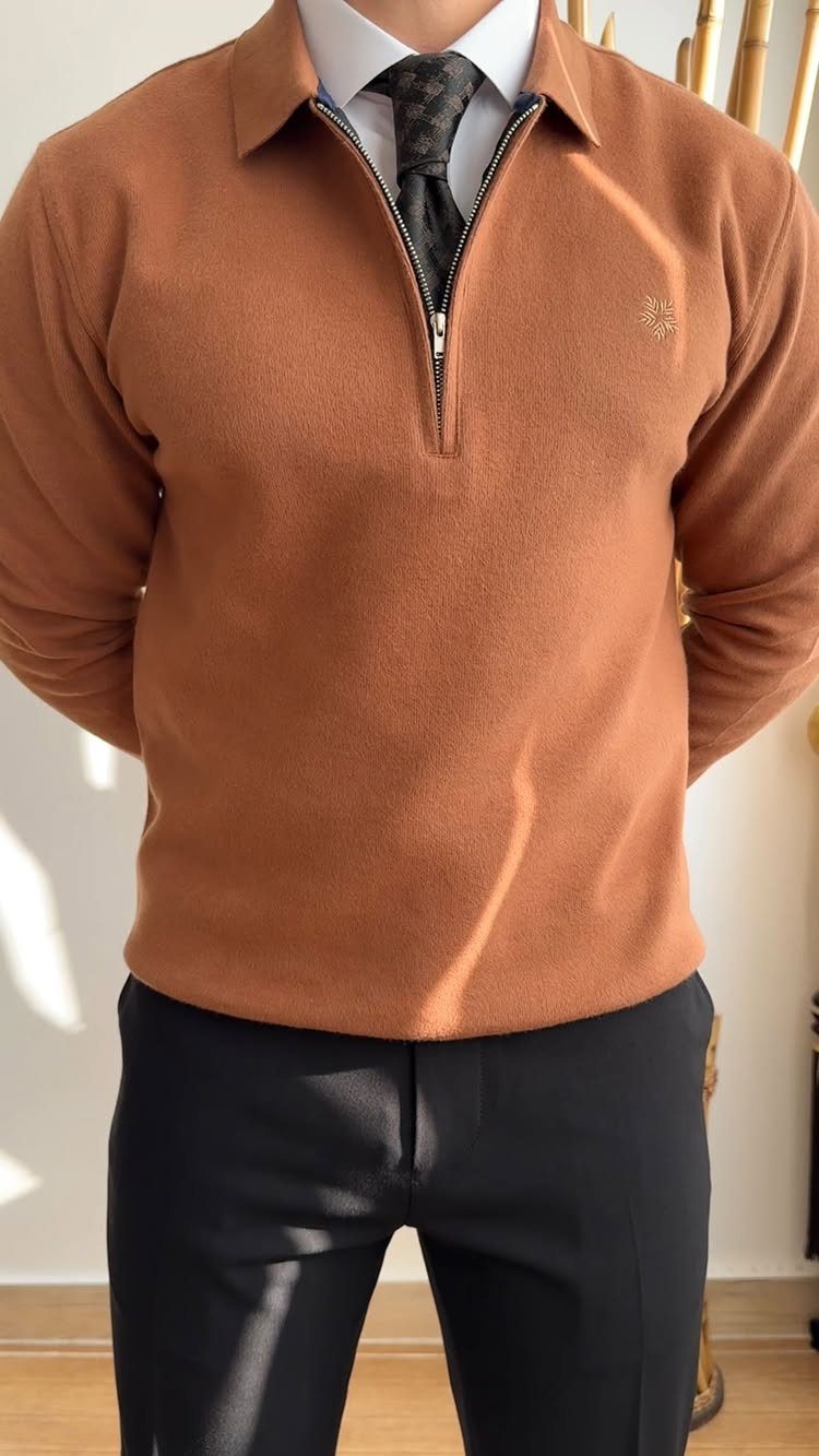 Man wearing a brown quarter-zip sweater, white shirt, patterned tie, and black trousers.