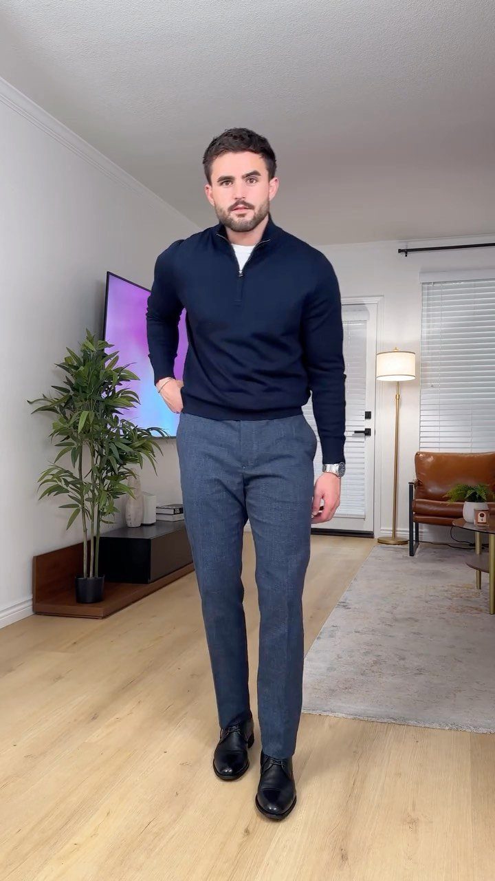 A man posing in a navy quarter-zip sweater, blue trousers, and black dress shoes.
