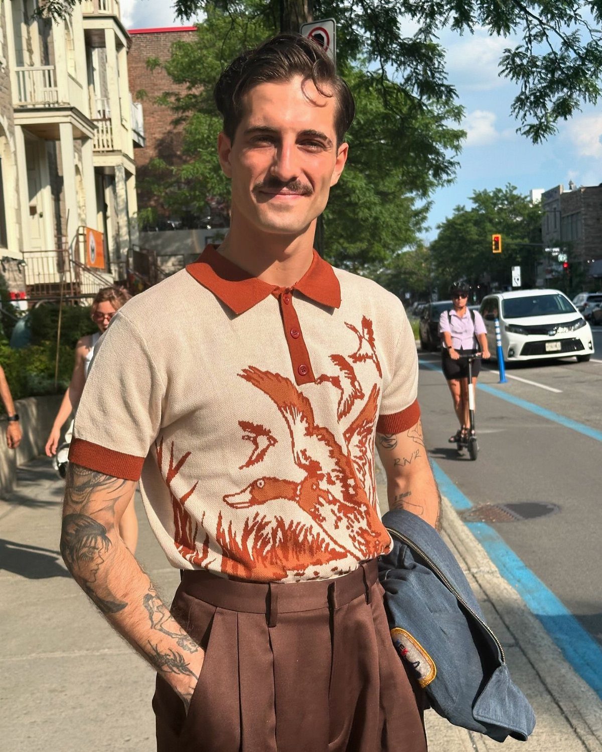 Man with a mustache wearing a vintage-style knit polo shirt with a duck graphic.
