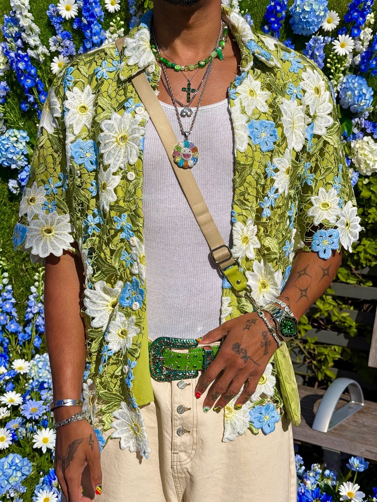 A person wearing a lime green floral appliqué shirt, white tank top, and cream trousers.