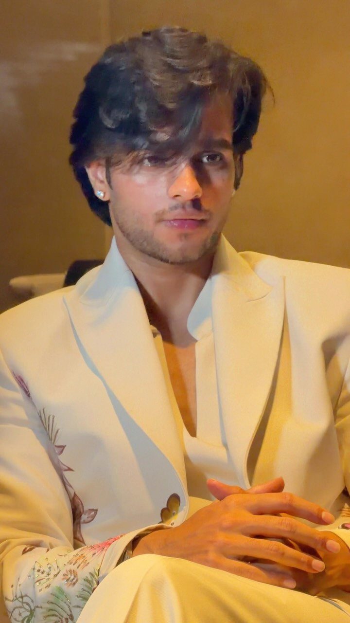 A young man wearing a cream suit with floral embroidery on the sleeve.