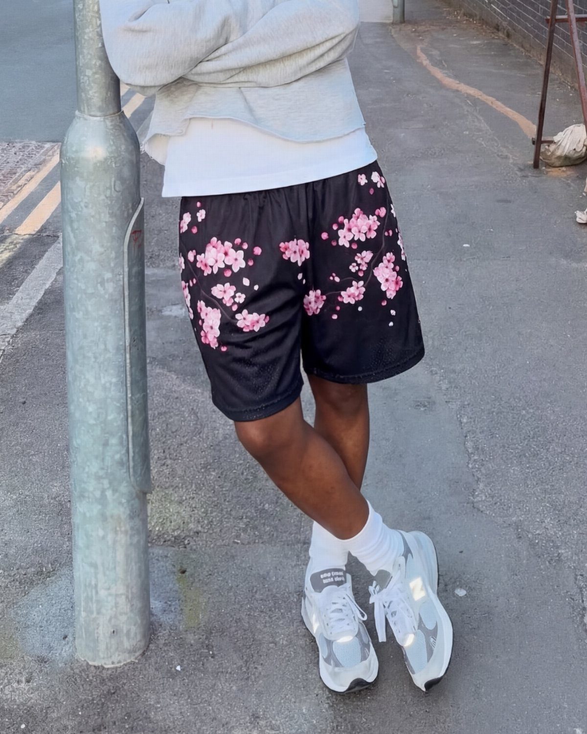 Person wearing black shorts with pink floral cherry blossom patterns and white sneakers.