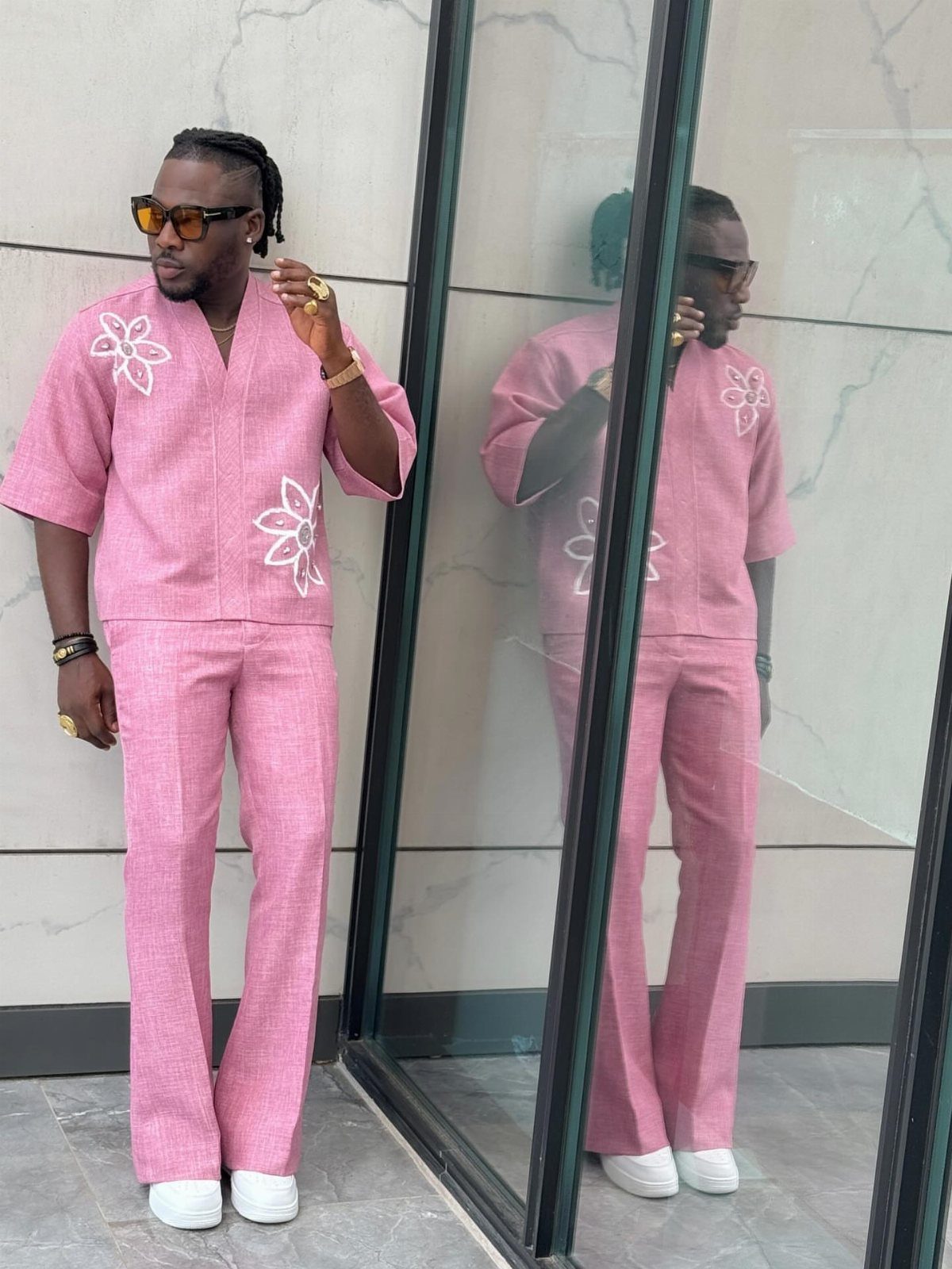 Man in a pink linen outfit with white floral embroidery standing next to a mirror.