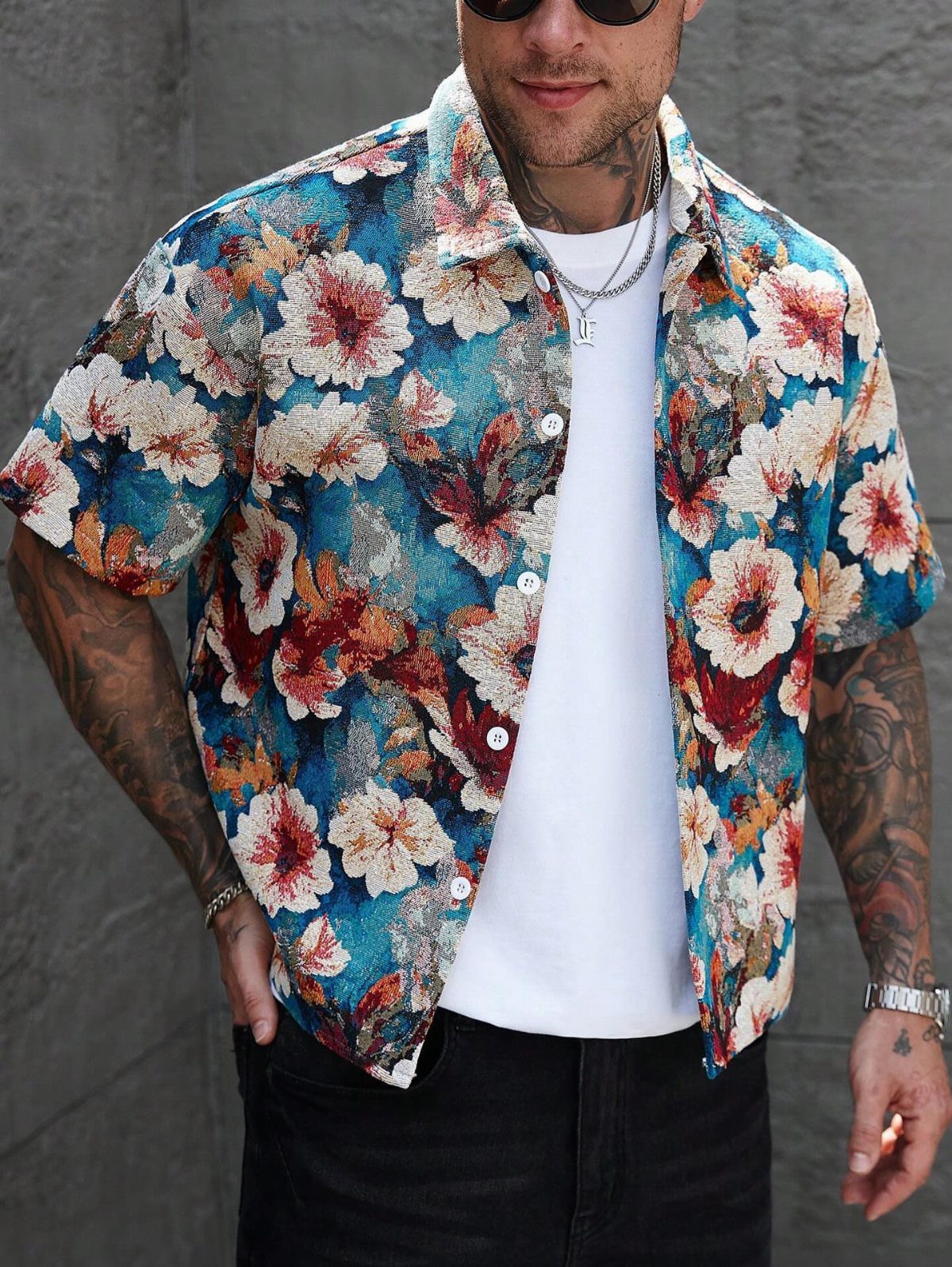 Man wearing a colorful floral print short-sleeved shirt over a white t-shirt and black jeans.