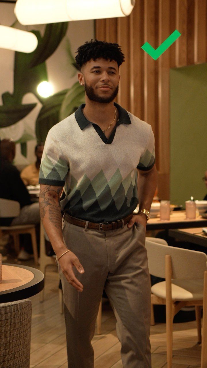 A stylish man wearing a patterned polo shirt and tan trousers walking through a restaurant.