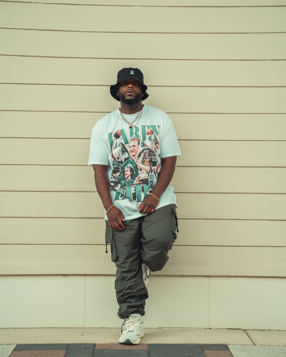 Man in a white graphic t-shirt, dark cargo pants, and a black bucket hat.