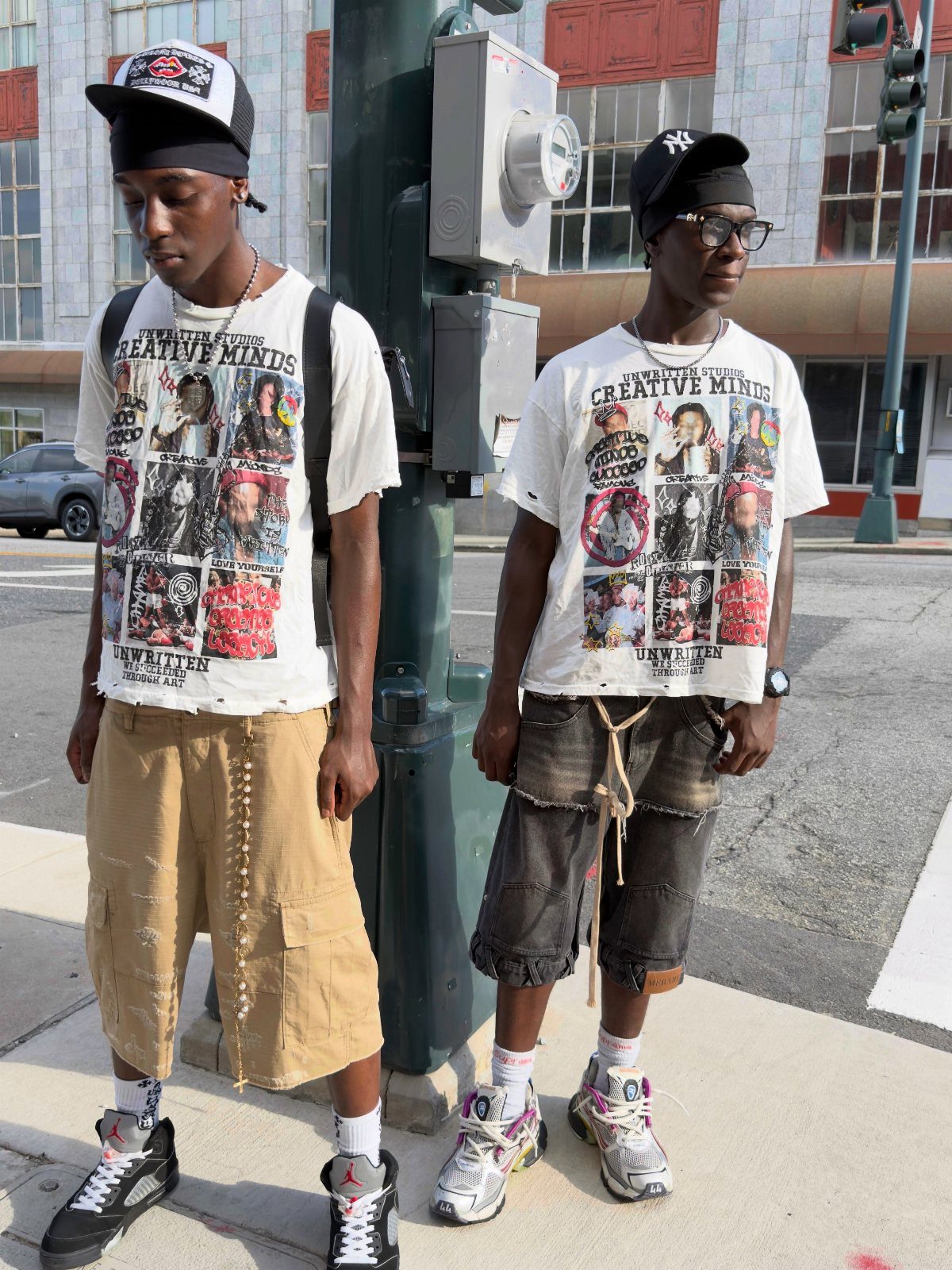 Two men wearing white graphic t-shirts and cargo shorts standing on a city street.