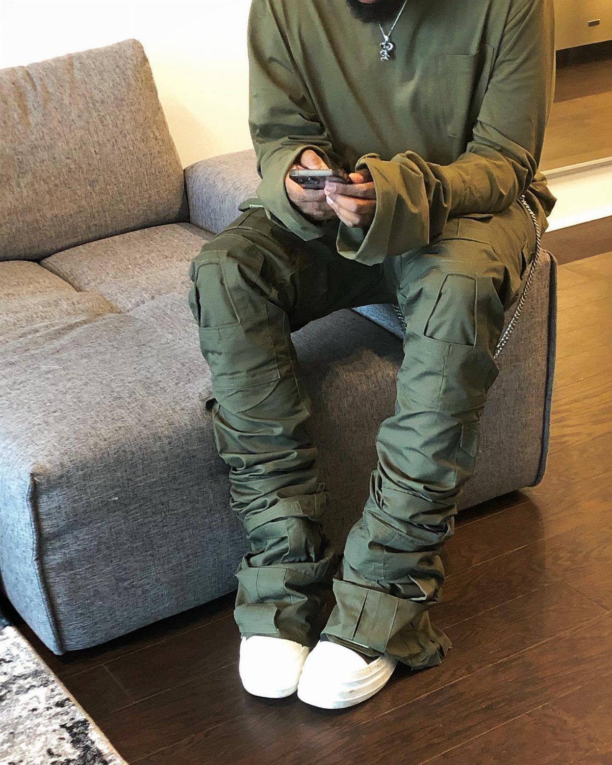 Person sitting on a grey sofa wearing olive green cargo pants and a matching long-sleeved shirt.