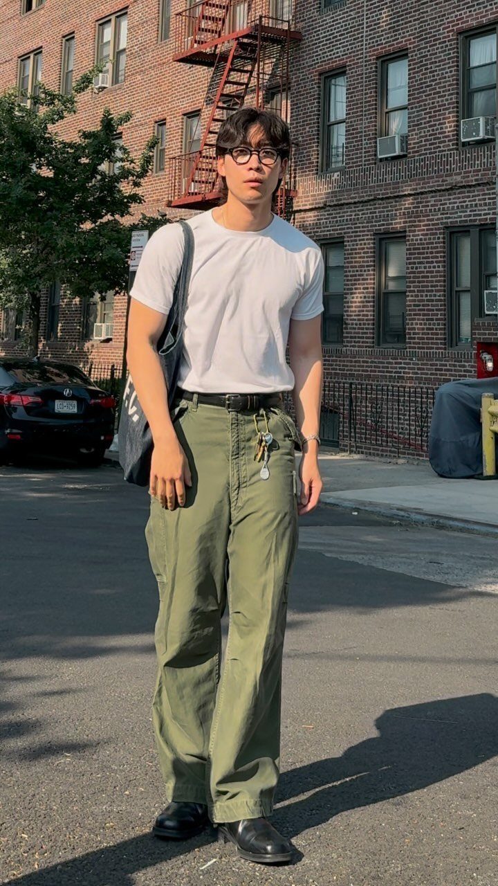 A man wearing a white t-shirt and olive green cargo pants standing on a city street.