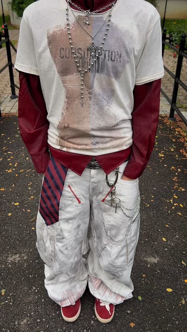 A person wearing layered grunge streetwear including a graphic tee, maroon sleeves, baggy cargo pants, and a tie.
