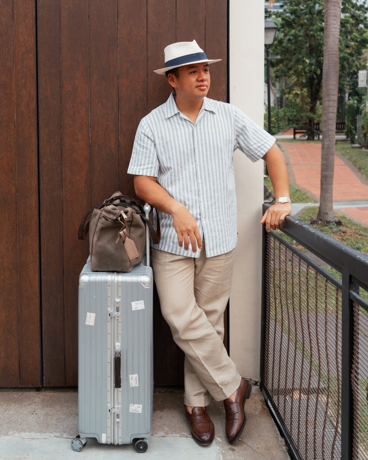 Man in a striped shirt and beige pants wearing a white Panama hat while leaning against a door.