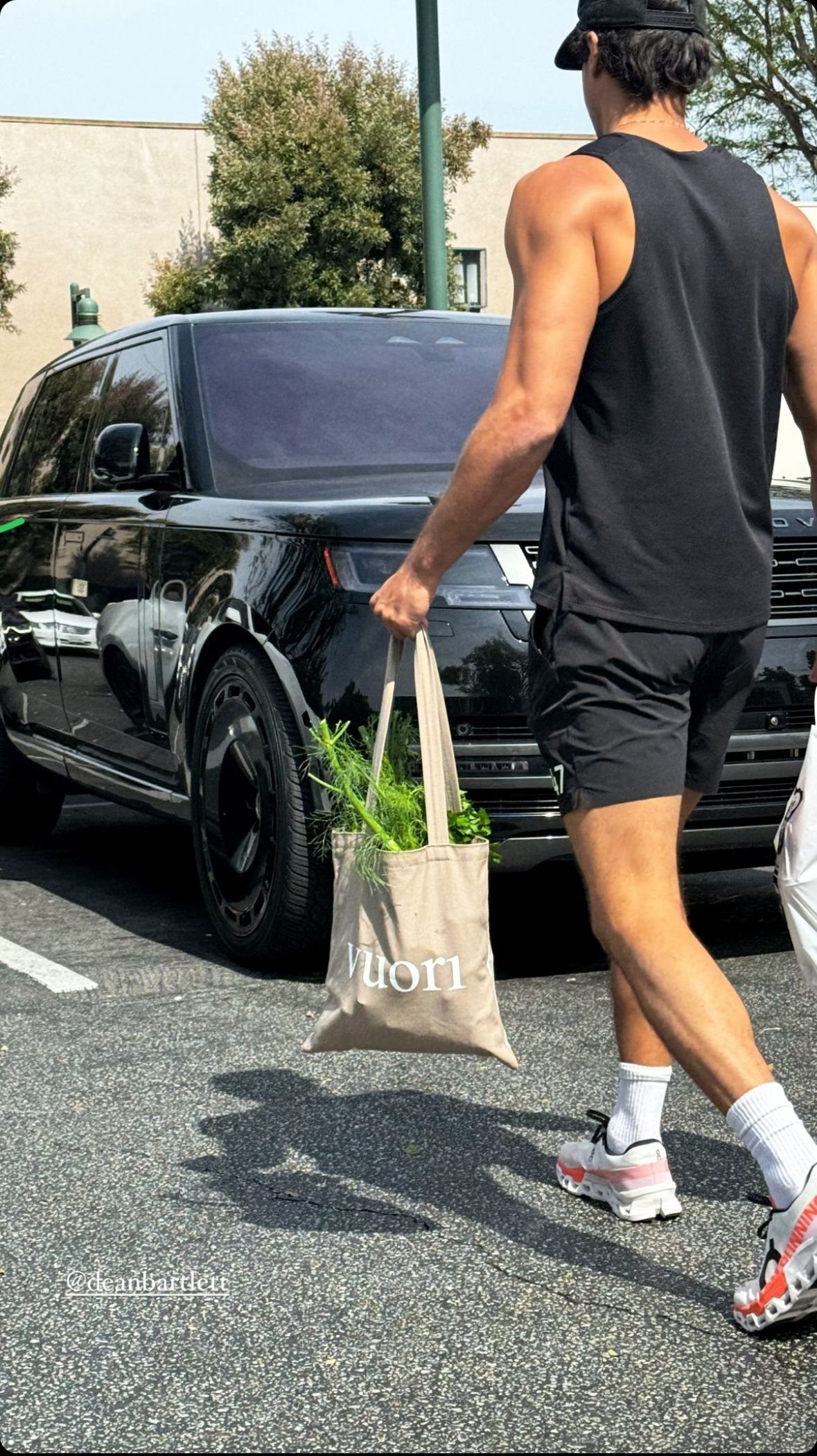 Man in an all-black athletic ensemble walking past a black SUV in a parking lot.