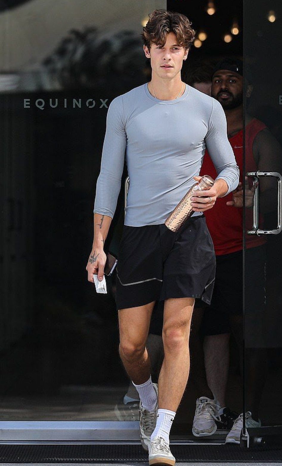 A man in a light blue long-sleeved shirt and black shorts walking out of a building.