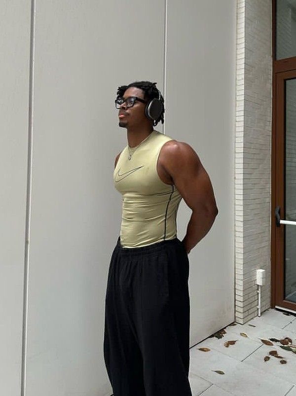 A man in a yellow Nike tank top and black athletic pants standing against a white wall.