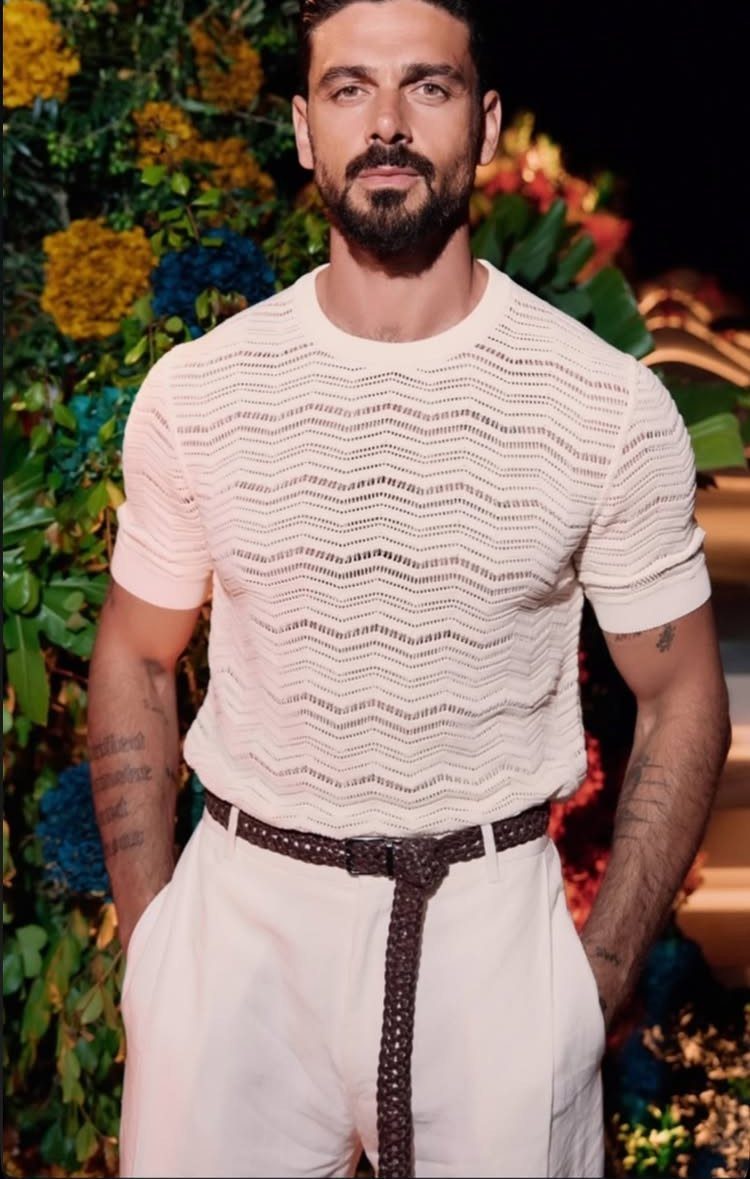 Man in a white textured knit shirt and white trousers with a braided belt.