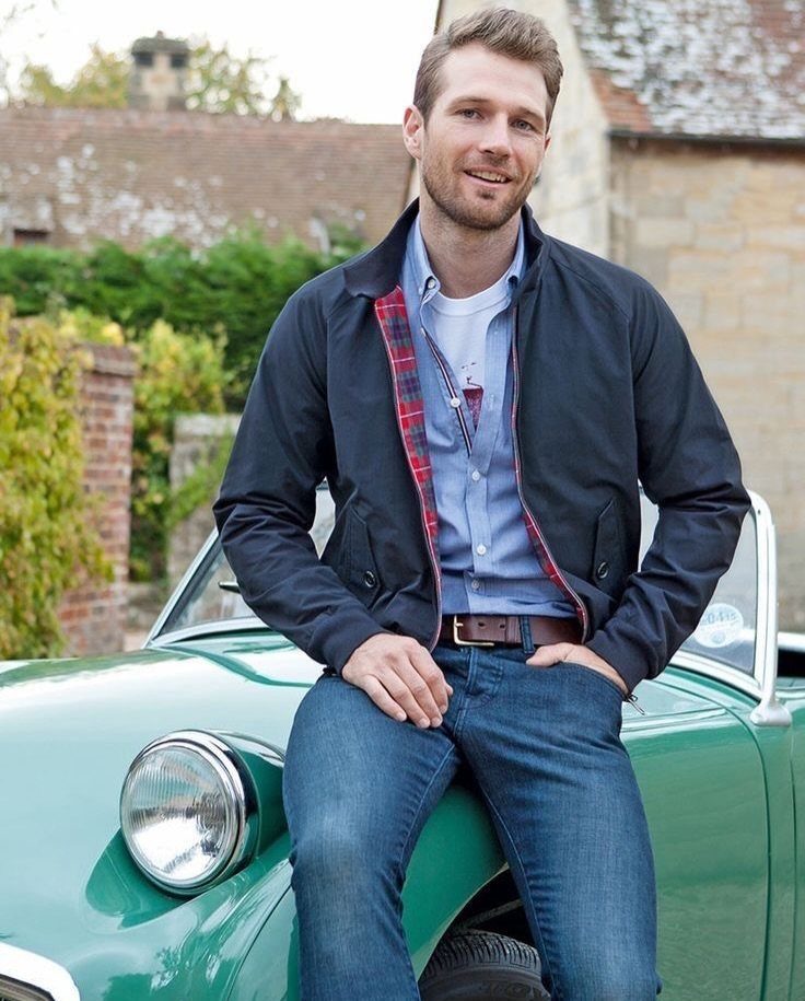 A man in a navy jacket and blue button-down shirt sitting on a green vintage car.
