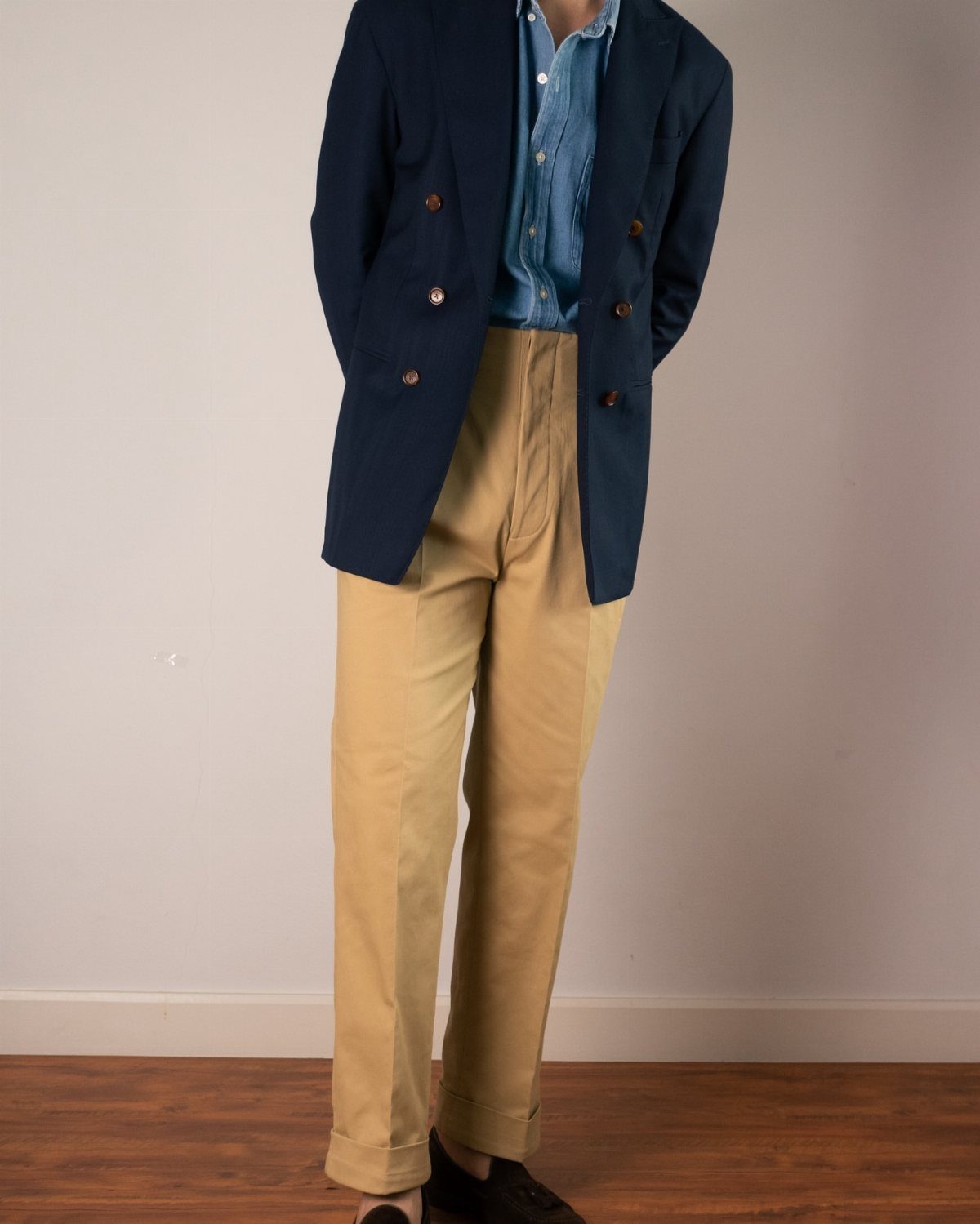 A person wearing a navy blazer, denim shirt, and tan khaki chino trousers.