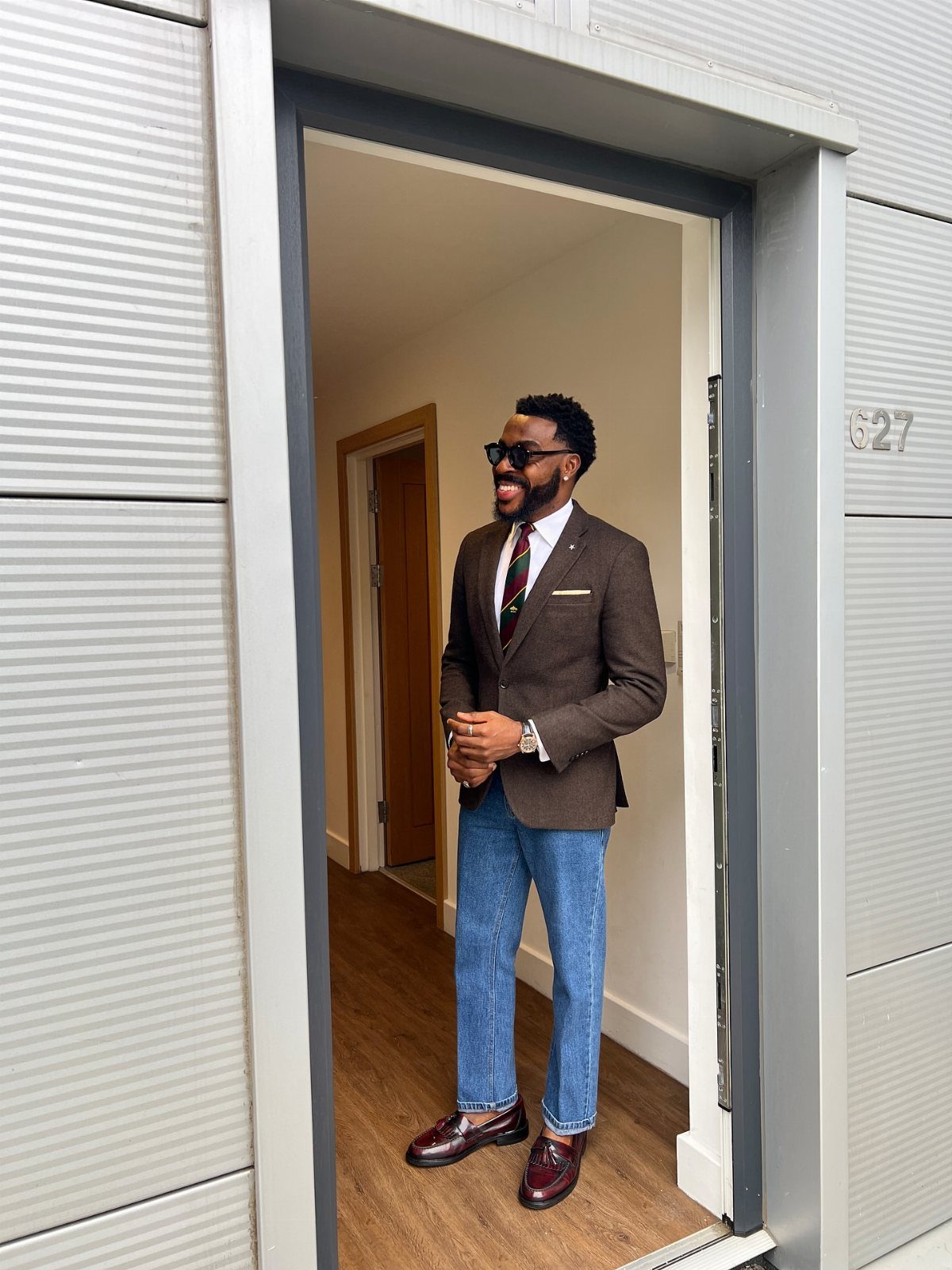 A man in a brown blazer and blue jeans wearing dark burgundy leather loafers.