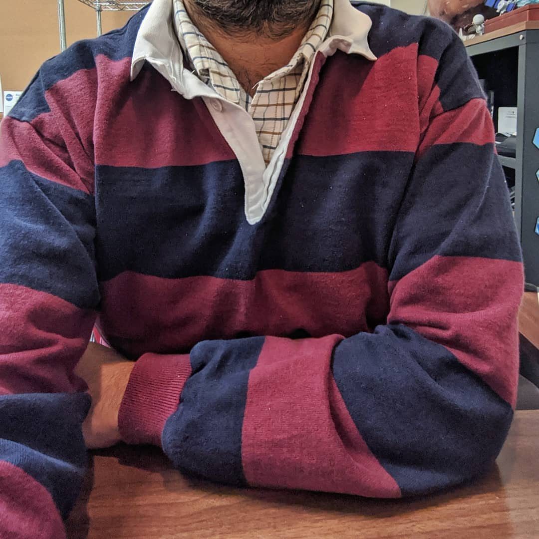 A person wearing a navy and burgundy striped rugby polo shirt with a white collar.