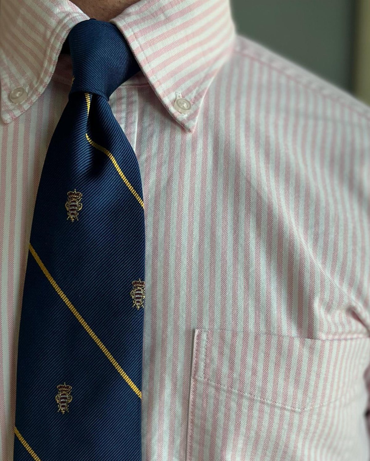 A person wearing a pink striped Oxford shirt and a navy blue patterned necktie.