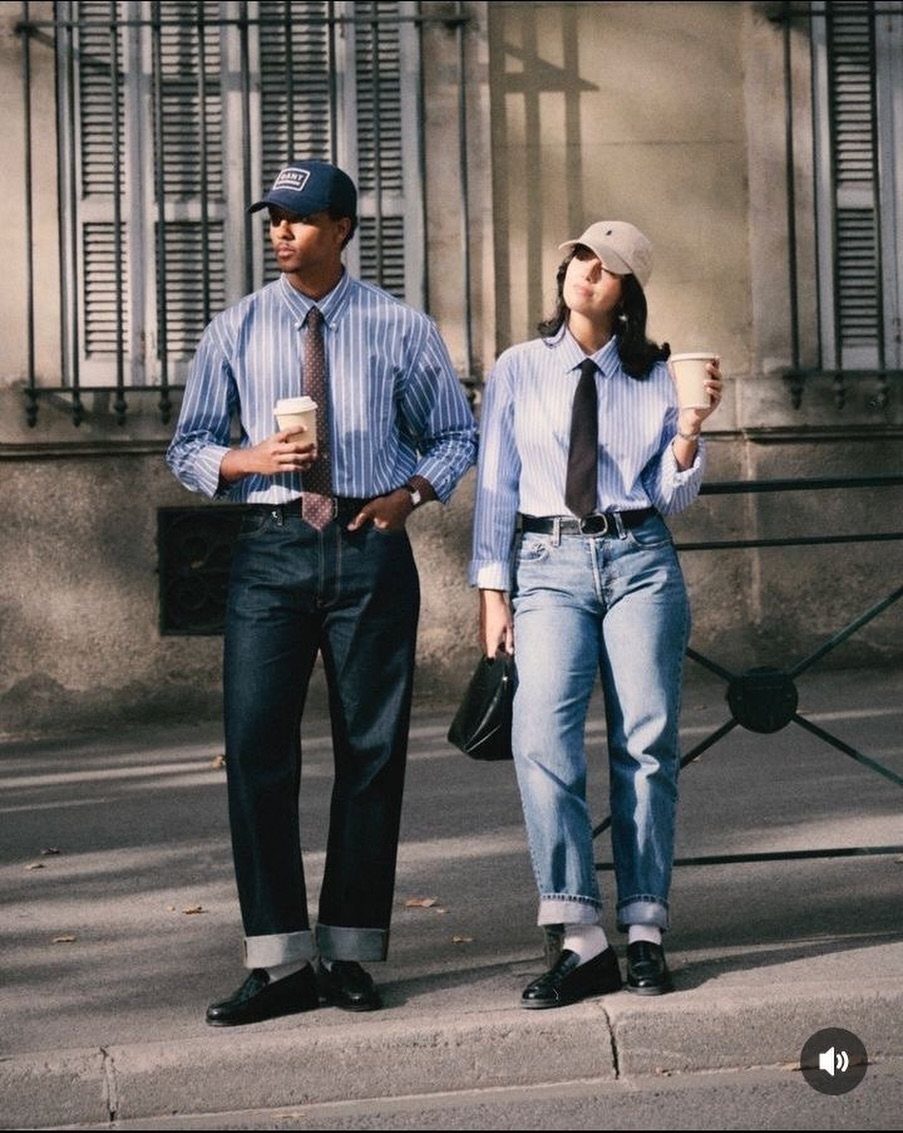 A man and woman walking in striped shirts, ties, and denim jeans on a city sidewalk.
