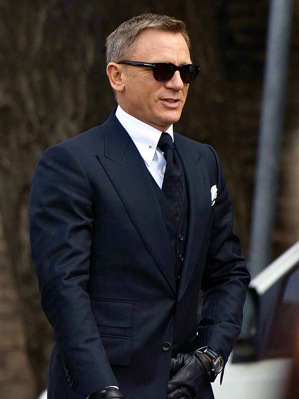 Daniel Craig in a navy suit wearing black sunglasses and a wristwatch.